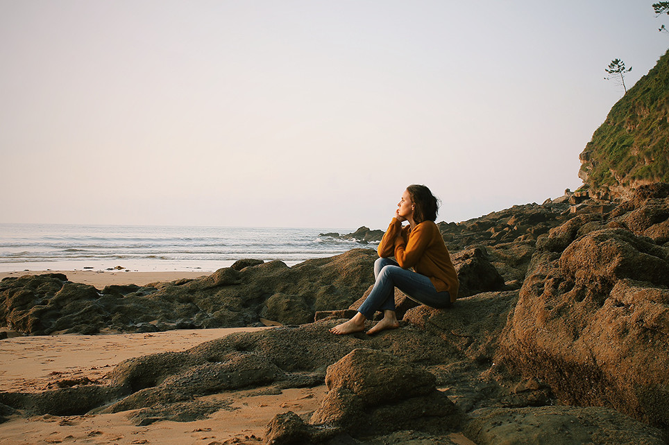 Žena sedí na pláži a rozmýšľa o živote